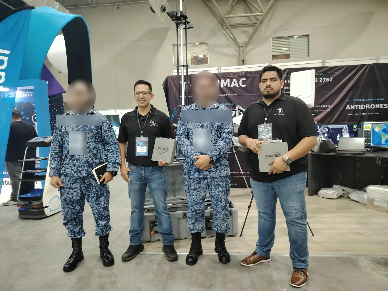 Personal de TECIMAC con visitantes uniformados en el stand; los rostros de los visitantes están difuminados