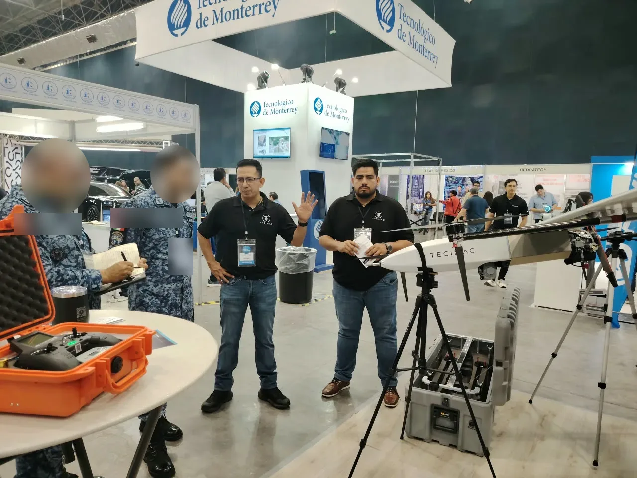 Personal de TECIMAC explicando el sistema a visitantes uniformados, con los rostros de los visitantes difuminados
